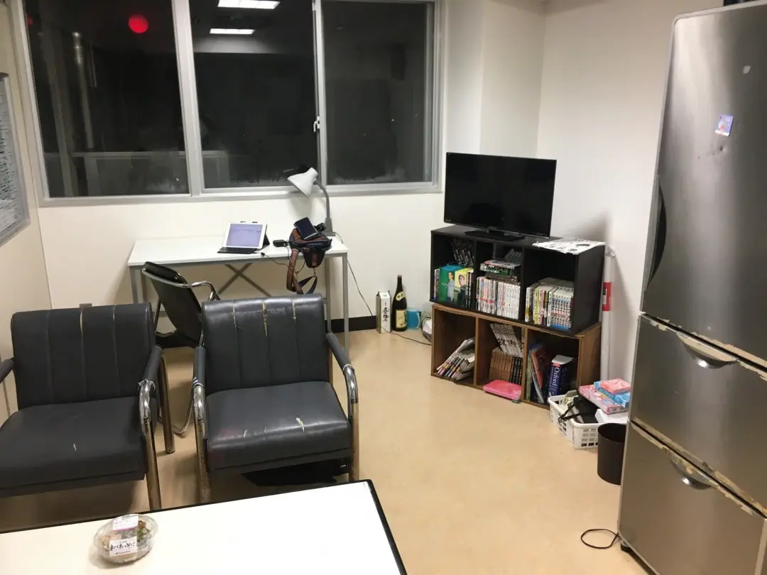 本棚二つの上にテレビ。腰掛け椅子の前に細長机、冷蔵庫